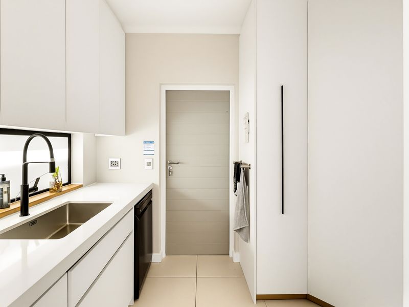 A modern, minimalist scullery featuring sleek white cabinetry, stone countertops, an undermount sink with a black mixer tap, and integrated dishwasher.
