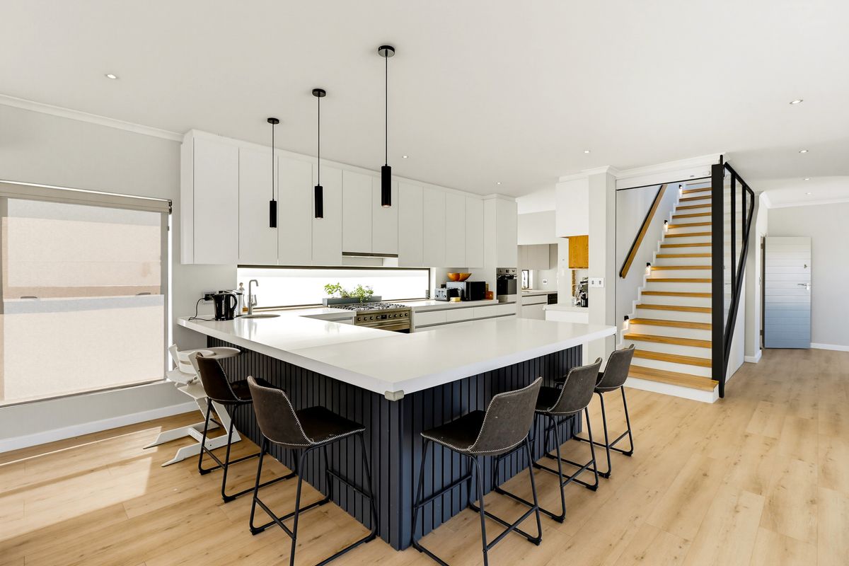 Modern open-plan kitchen featuring a large island with stone countertops, sleek cabinetry, integrated appliances, and a staircase leading to the upper level.
