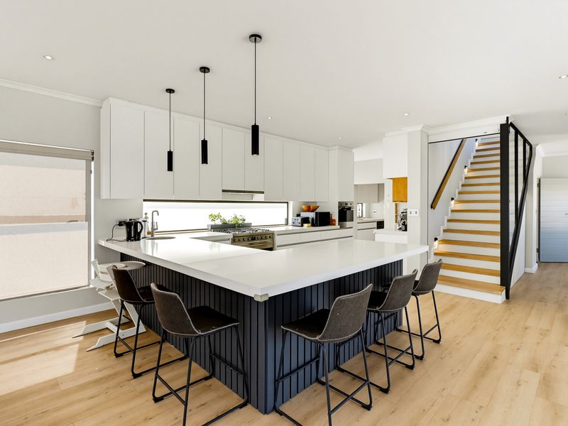 Modern open-plan kitchen featuring a large island with stone countertops, sleek cabinetry, integrated appliances, and a staircase leading to the upper level.