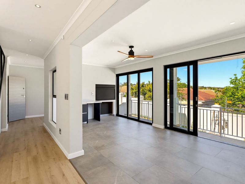 Spacious open-plan living area featuring modern tiled flooring, recessed lighting, a ceiling fan, and large sliding doors opening onto a balcony with scenic views.