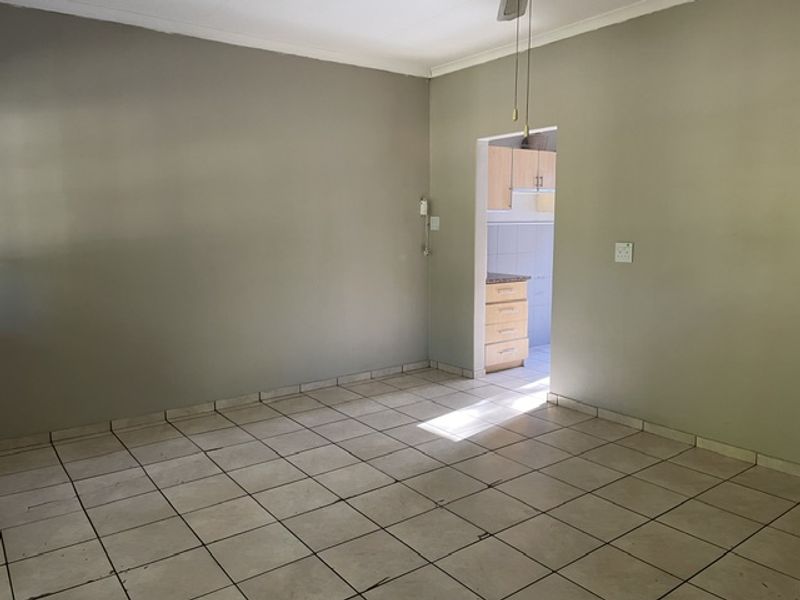 An empty living room featuring neutral painted walls and tiled flooring, with a direct view into the adjacent kitchen area.