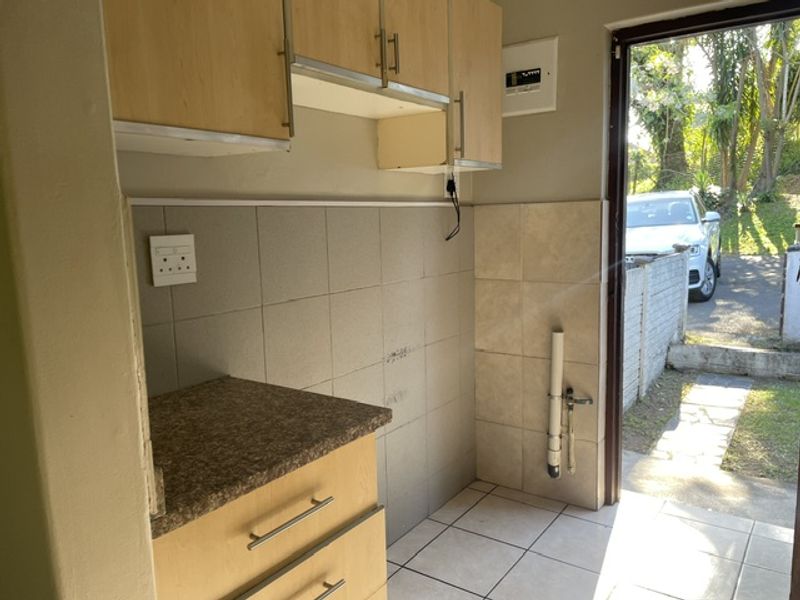 A functional laundry area featuring laminate cabinetry, tiled splashbacks, and direct access to the exterior, providing a practical space for utility and washing needs.