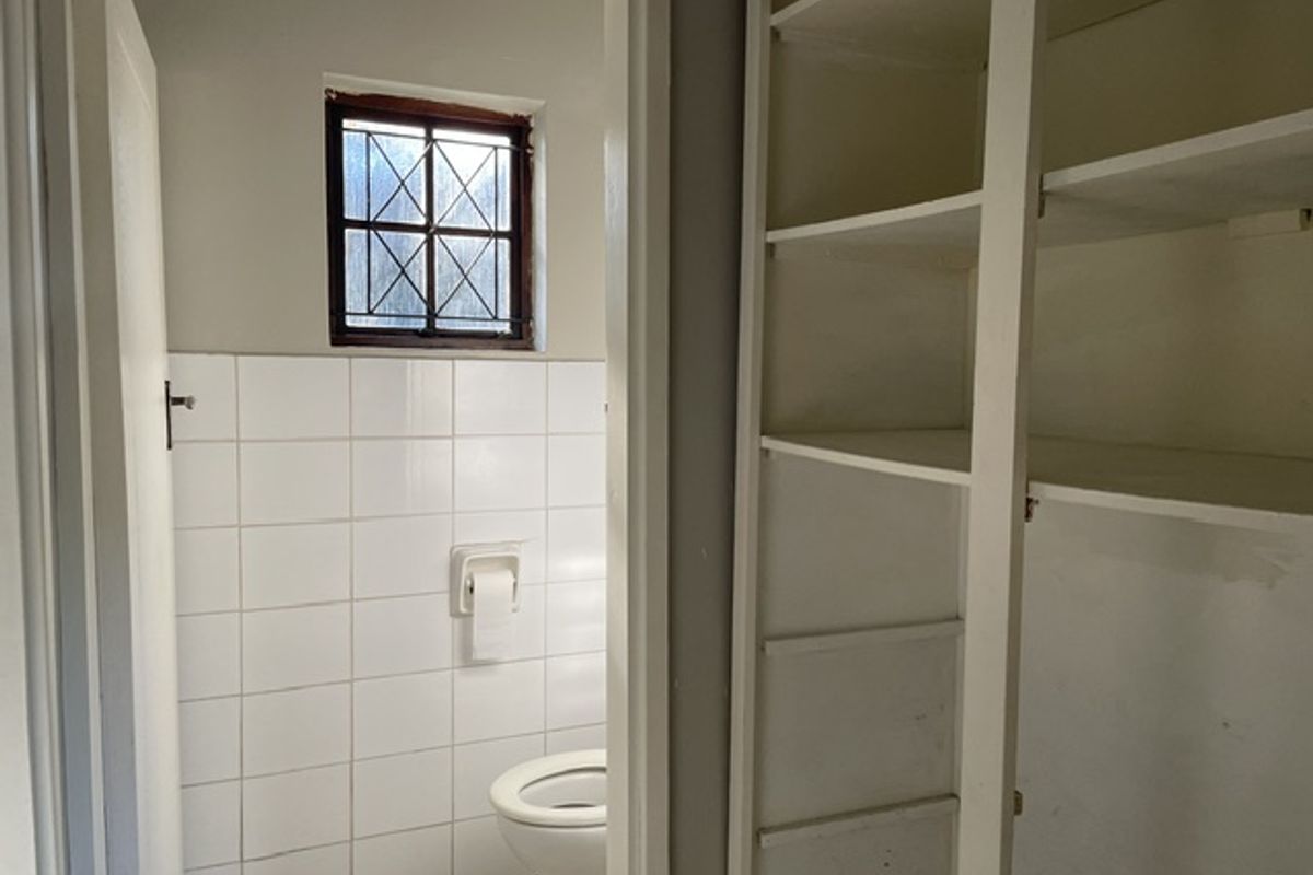 A functional bathroom featuring tiled walls, a toilet, and built-in storage shelving, providing a practical layout with potential for cosmetic updates.