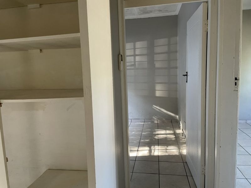 A vacant hallway featuring tiled flooring and built-in shelving, leading into an adjacent room with natural light.