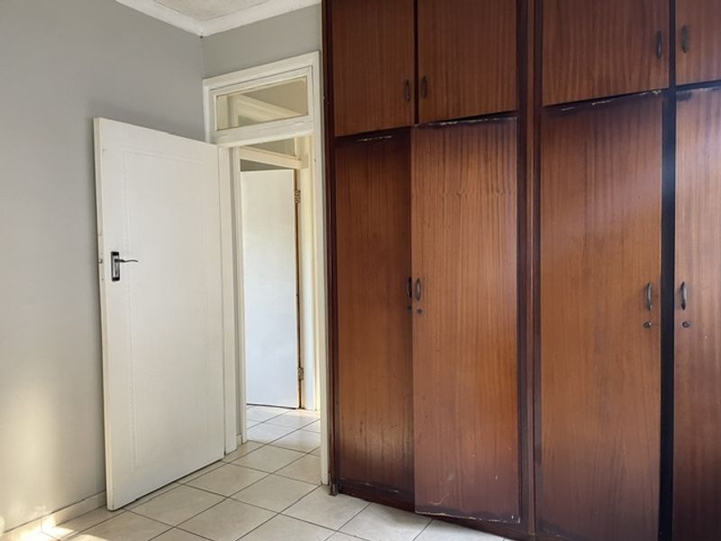 A bedroom featuring built-in wooden cupboards and tiled flooring, offering a functional space ready for personalization.