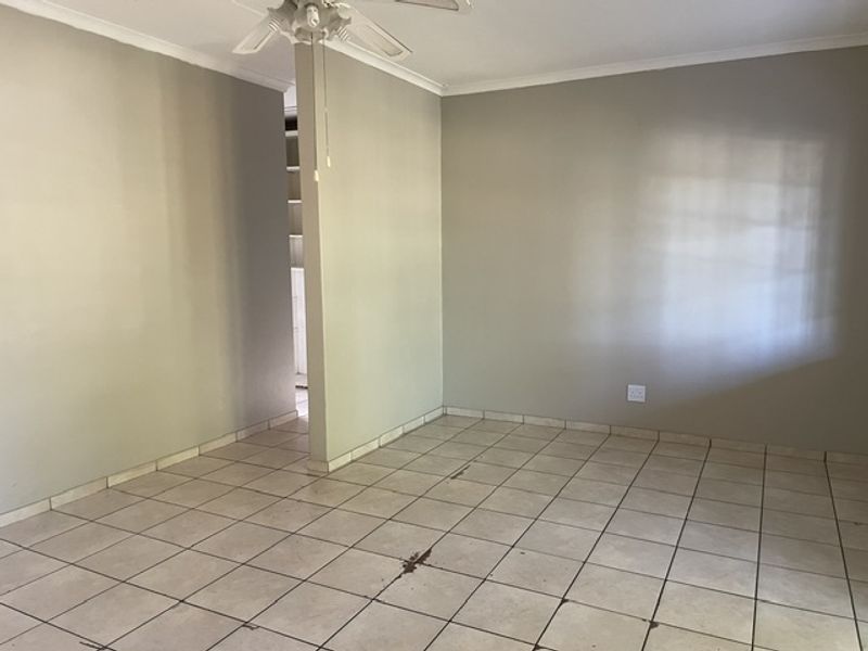 An empty living area featuring neutral wall paint, a ceiling fan, and ceramic tiled flooring with some visible wear.