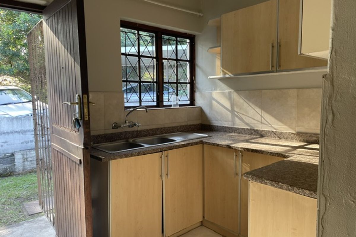 A functional kitchen featuring laminate cabinetry, double bowl stainless steel sink, tiled backsplash, and direct access to the exterior.