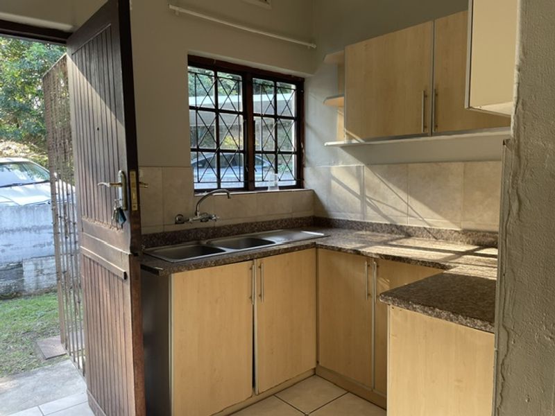 A functional kitchen featuring laminate cabinetry, double bowl stainless steel sink, tiled backsplash, and direct access to the exterior.