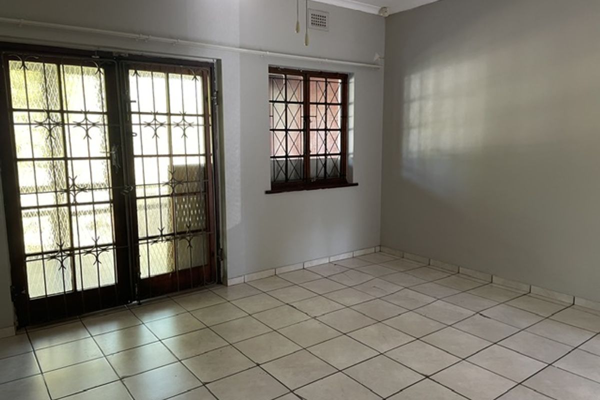 A bright, empty living room featuring tiled flooring, a ceiling fan, and secure double doors leading to an outdoor area.