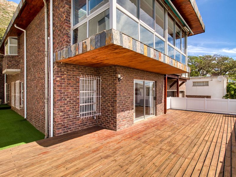 Spacious outdoor timber deck area featuring exposed brick walls, sliding glass doors, and a covered section with slate detailing.