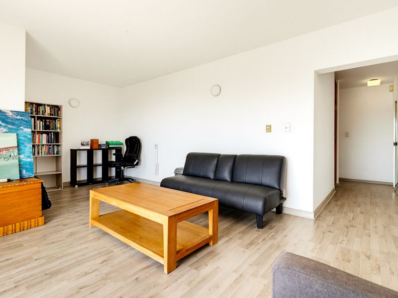 A bright living room featuring light-toned laminate flooring and a built-in shelving unit, offering a neutral canvas for interior design.