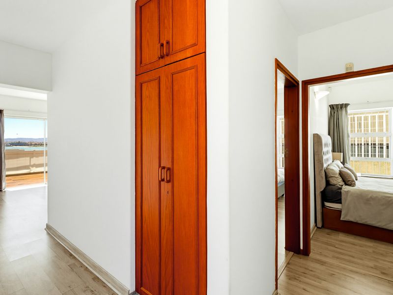 A bright hallway featuring light laminate flooring and a tall, built-in wooden storage cupboard, providing access to adjacent rooms.