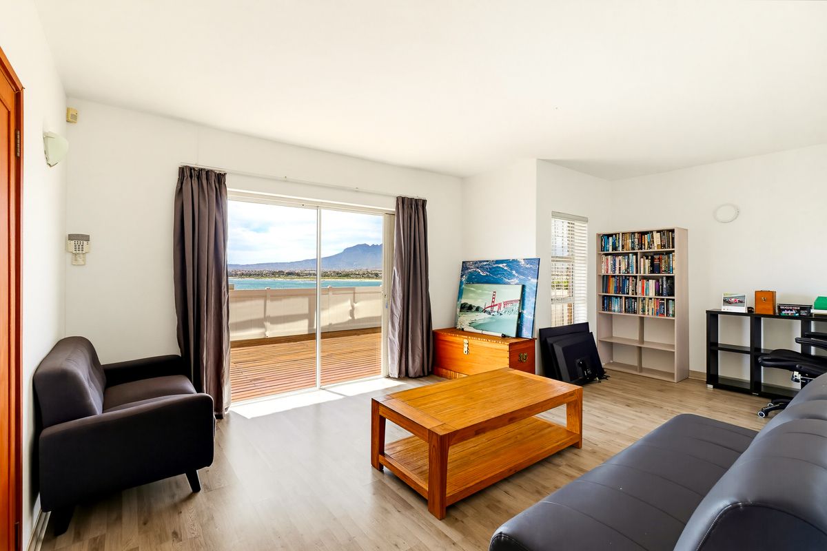 Bright living room featuring light laminate flooring and a large sliding glass door that opens onto a balcony with scenic water and mountain views.