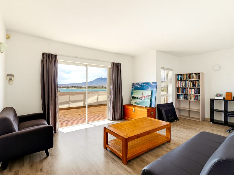 Bright living room featuring light laminate flooring and a large sliding glass door that opens onto a balcony with scenic water and mountain views.