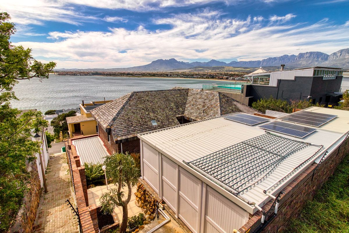 Aerial view of the property featuring solar panels, a slate roof, and a scenic coastal and mountain backdrop.