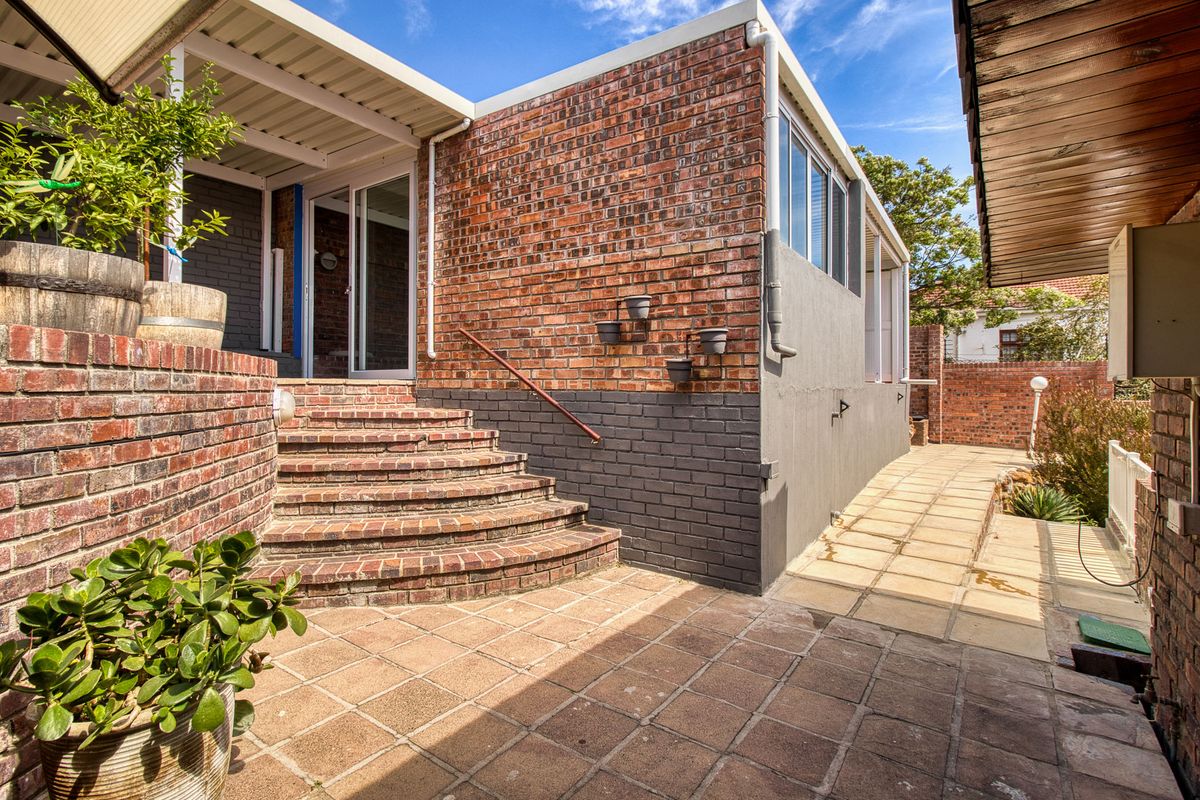 Rear exterior view featuring a paved patio area, brick staircase leading to a sliding glass door, and a covered patio section.