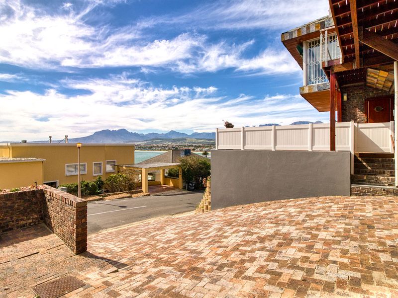 Front exterior view featuring a brick paved driveway, retaining walls, and an elevated entrance with scenic mountain and coastal views.