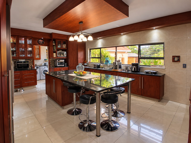 Spacious kitchen featuring rich wooden cabinetry, a large granite-topped island, polished tile flooring, and integrated appliances with ample natural light.