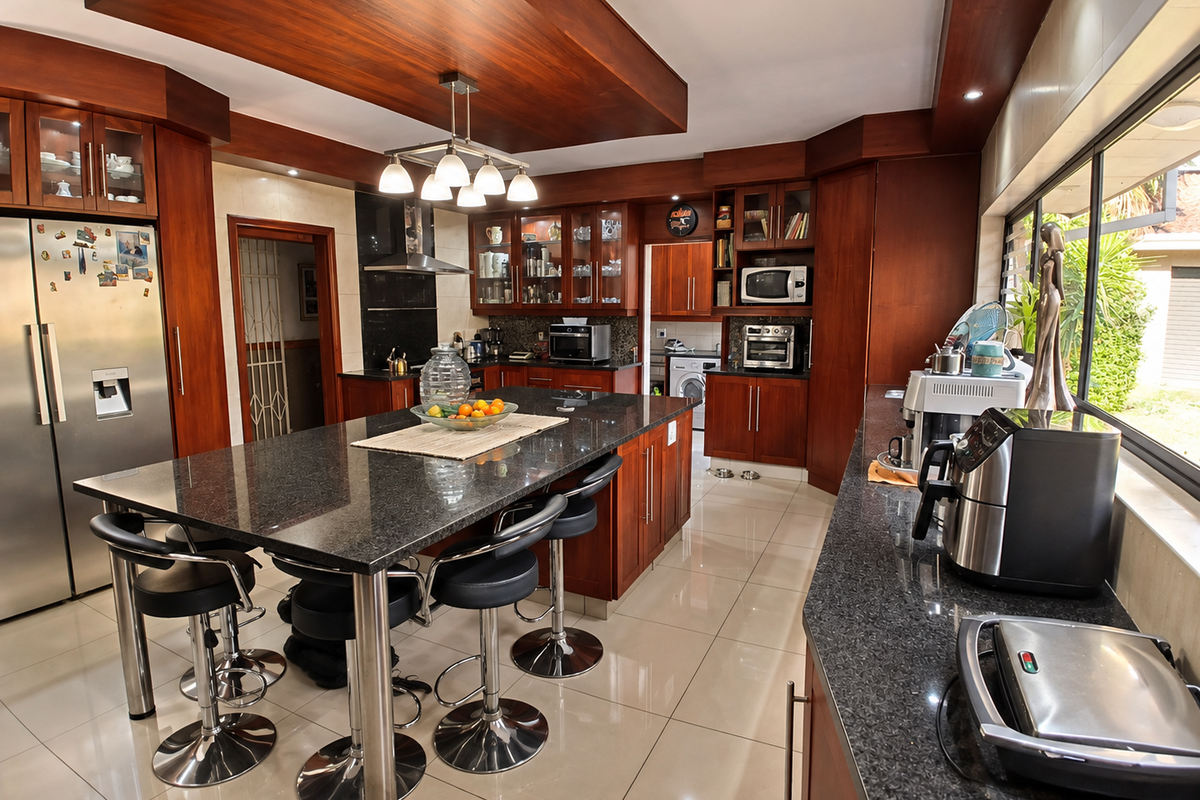 Spacious kitchen featuring dark granite countertops, extensive wooden cabinetry, a central island with seating, and a dedicated scullery area with modern finishes.