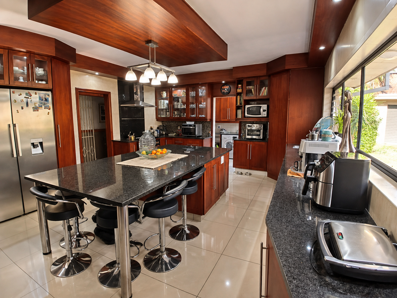 Spacious kitchen featuring dark granite countertops, extensive wooden cabinetry, a central island with seating, and a dedicated scullery area with modern finishes.