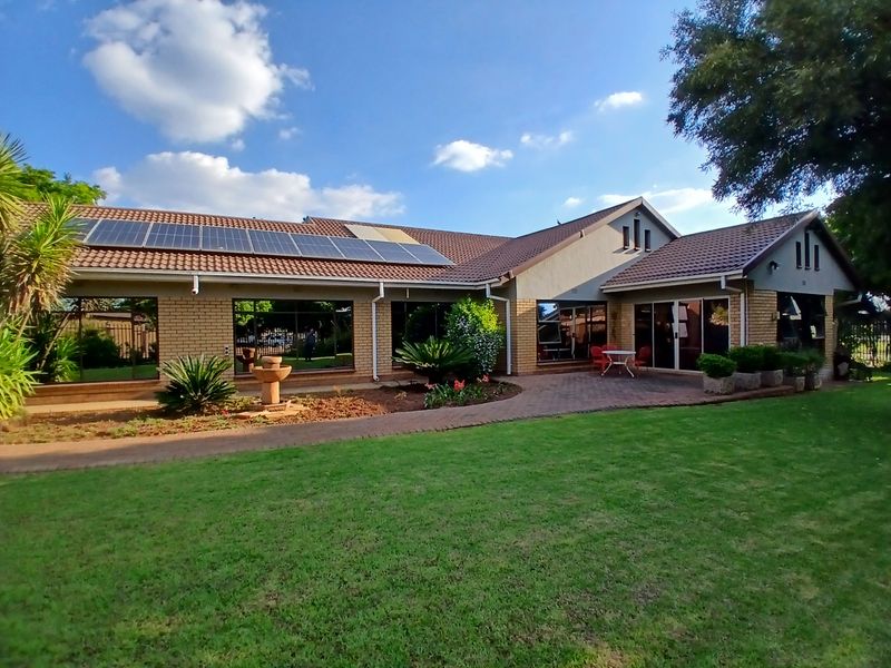Rear view of the house featuring a well-maintained lawn, paved walkway, brick exterior, and roof-mounted solar panels.