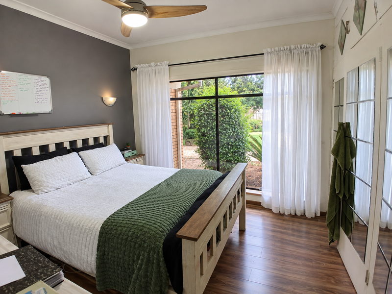 A well-maintained bedroom featuring laminate flooring, a ceiling fan, and a large sliding glass door providing direct access to the garden.