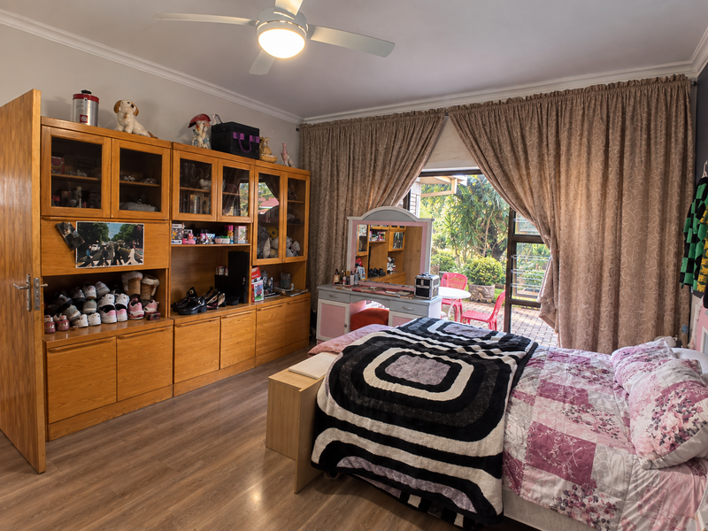 A spacious bedroom featuring laminate flooring, a ceiling fan, and extensive built-in wooden cabinetry, with direct access to an outdoor patio area.