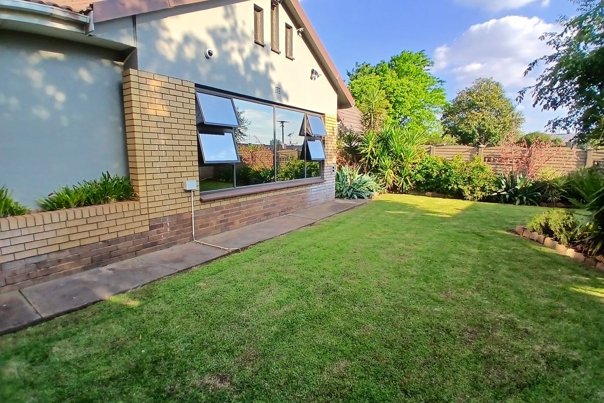 A well-maintained rear exterior view of the house featuring a brick facade, large top-hung windows, a concrete walkway, and a neat garden.