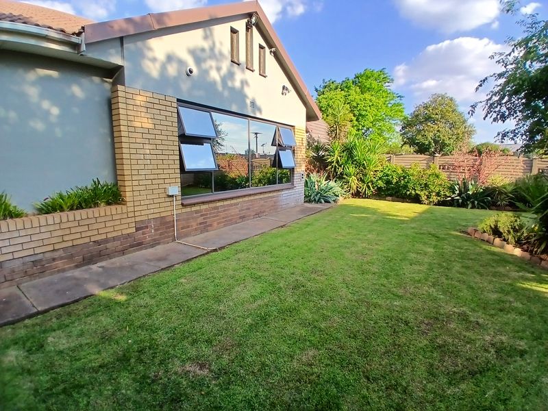 A well-maintained rear exterior view of the house featuring a brick facade, large top-hung windows, a concrete walkway, and a neat garden.