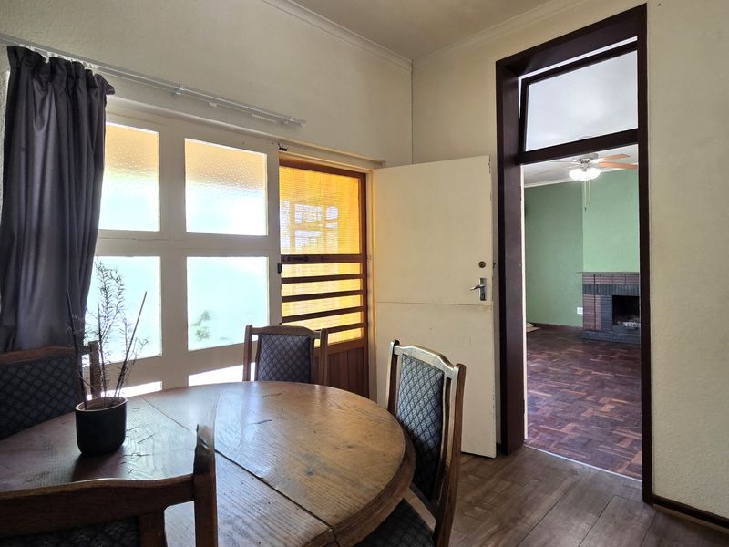Dining area featuring original wooden flooring and coved cornicing, with a view through to an adjacent living space with a fireplace.