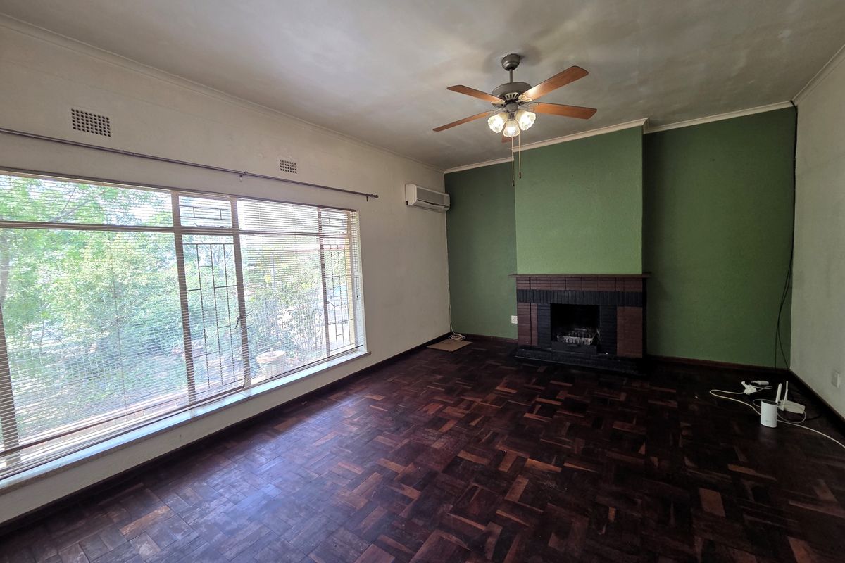 Spacious living room featuring original parquet flooring, a built-in fireplace, ceiling fan, and split-system air conditioning, offering a blank canvas for renovation.