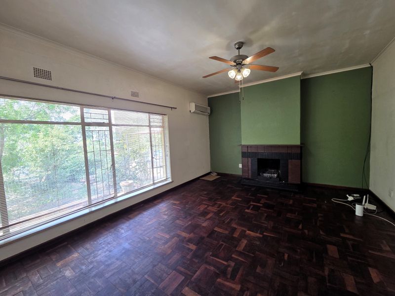 Spacious living room featuring original parquet flooring, a built-in fireplace, ceiling fan, and split-system air conditioning, offering a blank canvas for renovation.