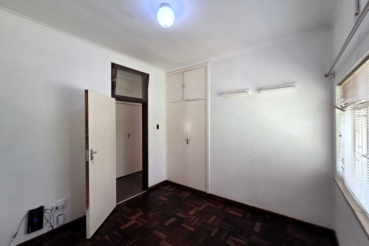 A vacant bedroom featuring classic parquet flooring, built-in cupboards, and a ceiling light fixture, offering a blank canvas for personalization.