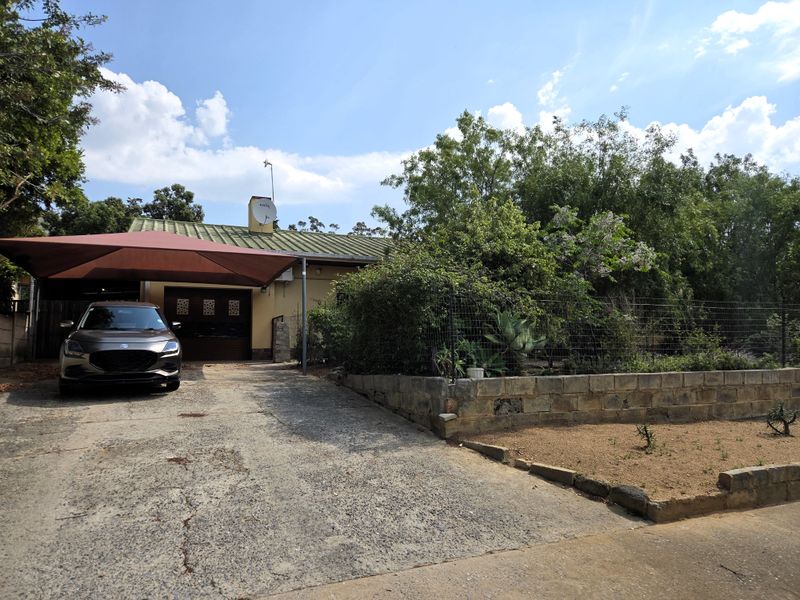 Front exterior view of the property featuring a concrete driveway, shade sail carport, and a metal roof with established garden surroundings.
