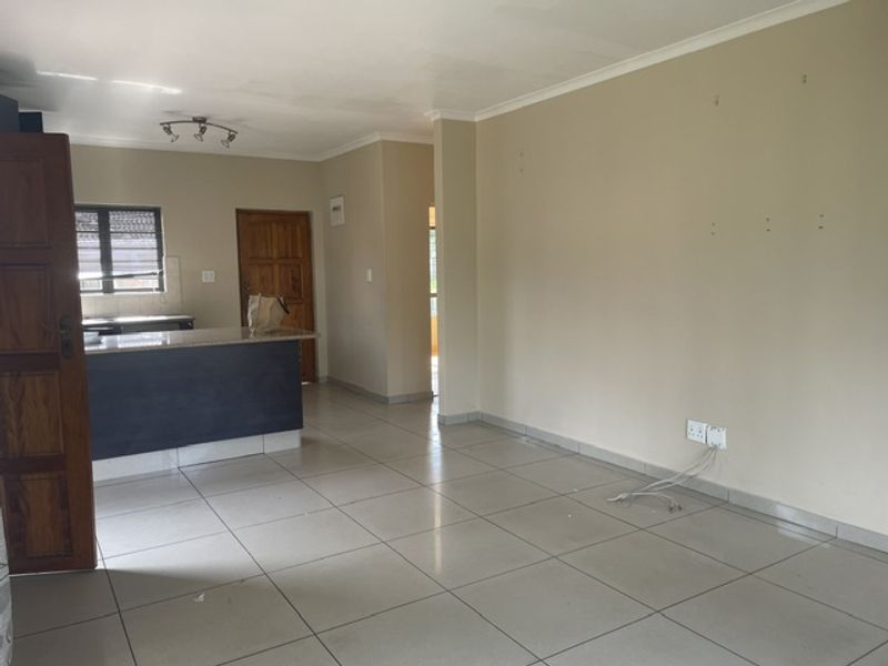 An open-plan living and kitchen area featuring tiled flooring, a kitchen island with granite countertops, and neutral wall finishes.