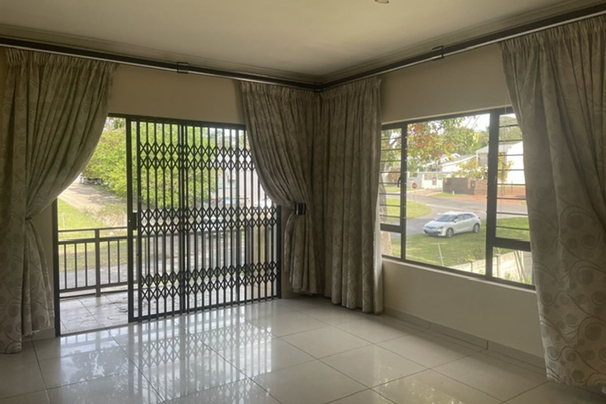 A bright and spacious living area featuring polished tiled floors, large windows for natural light, and a secure sliding gate leading to a balcony.