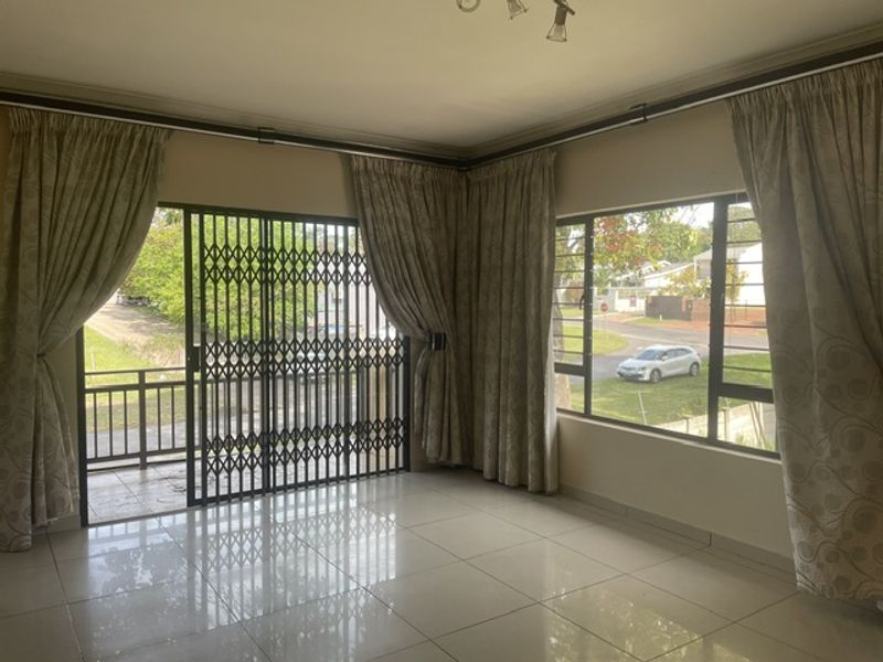 A bright and spacious living area featuring polished tiled floors, large windows for natural light, and a secure sliding gate leading to a balcony.