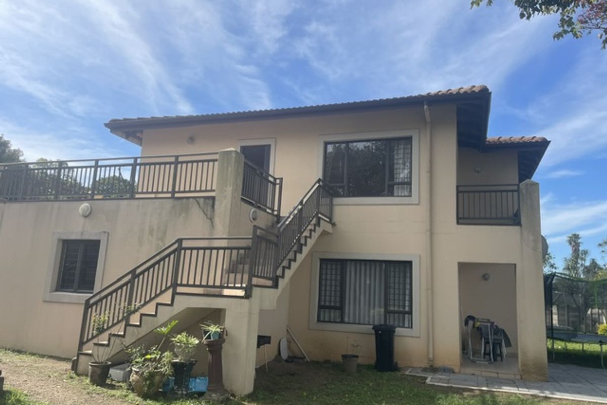 Rear view of a two-story apartment building featuring an external staircase, balcony, and tiled roof with visible exterior wall weathering.