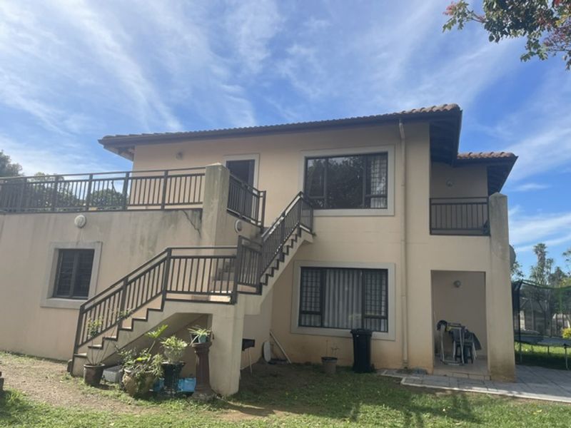 Rear view of a two-story apartment building featuring an external staircase, balcony, and tiled roof with visible exterior wall weathering.
