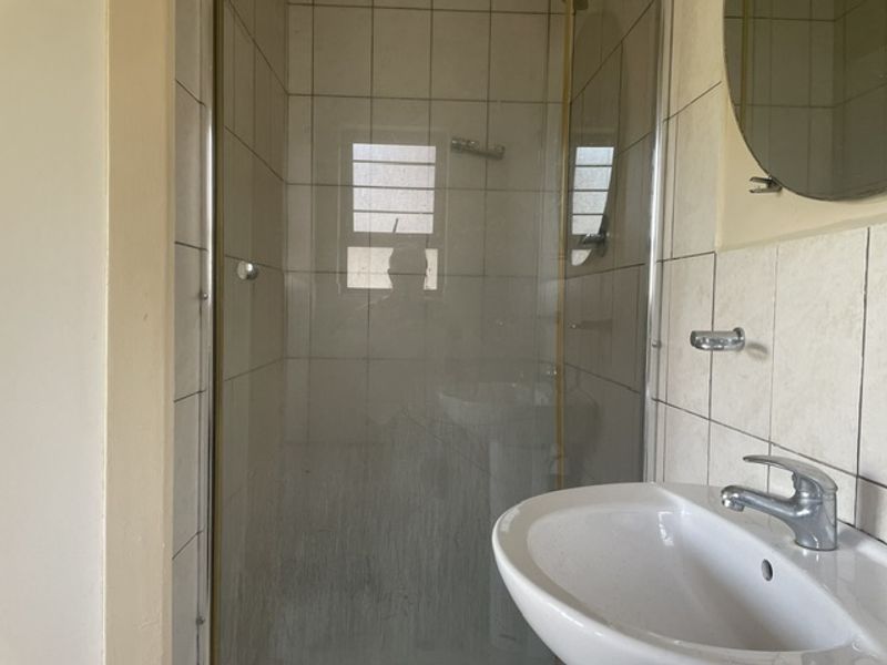 A compact bathroom featuring a shower enclosure with glass door, pedestal basin with mixer tap, and tiled wall finishes.