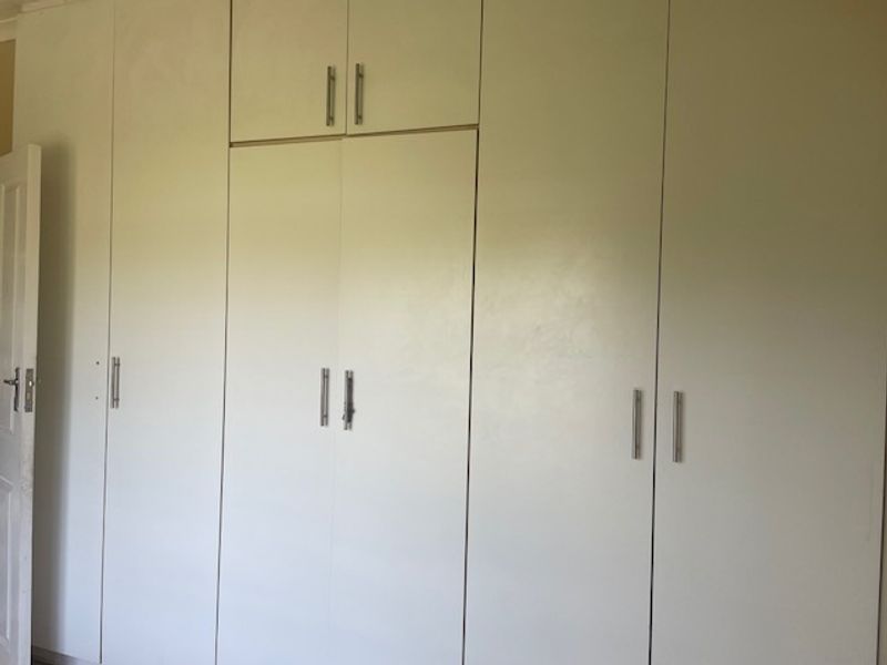 A bedroom featuring floor-to-ceiling built-in cupboards with modern handles, providing ample storage space.