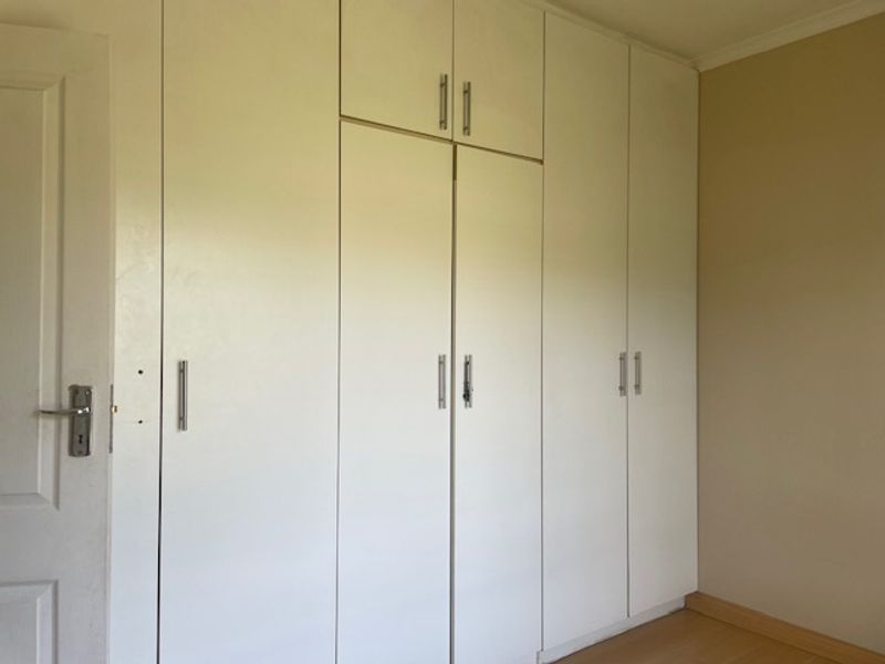 A bedroom featuring extensive white built-in cupboards with overhead storage and laminate flooring.