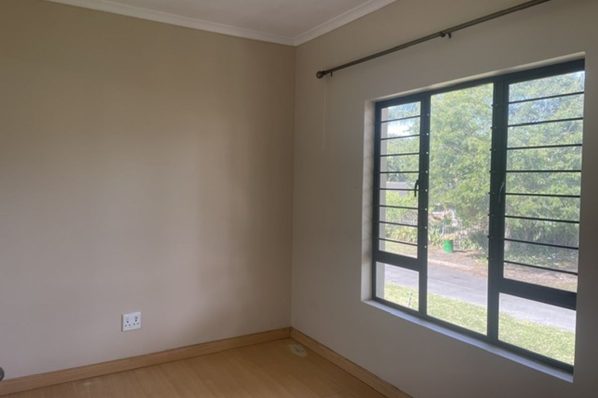 A bright, empty bedroom featuring laminate flooring, a large window with security bars, and neutral wall tones, ready for personalization.