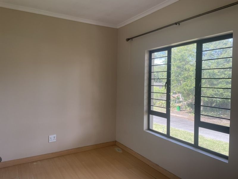 A bright, empty bedroom featuring laminate flooring, a large window with security bars, and neutral wall tones, ready for personalization.