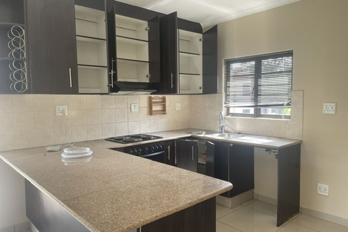 A functional kitchen featuring granite countertops, built-in cabinetry, a hob, oven, and tiled backsplash, offering a practical layout for daily use.