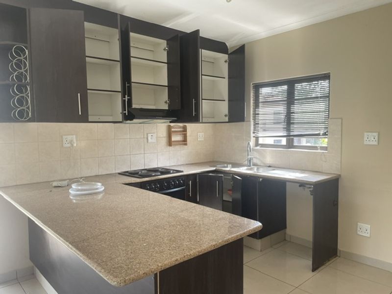 A functional kitchen featuring granite countertops, built-in cabinetry, a hob, oven, and tiled backsplash, offering a practical layout for daily use.