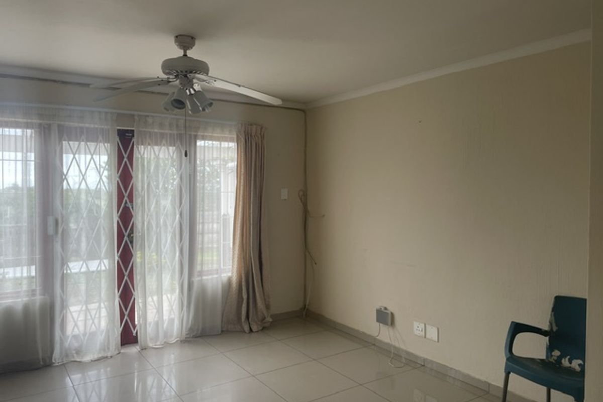 A spacious living area featuring tiled flooring, a ceiling fan, and a sliding glass door with a security gate leading to the exterior.