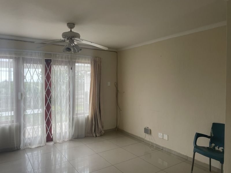 A spacious living area featuring tiled flooring, a ceiling fan, and a sliding glass door with a security gate leading to the exterior.