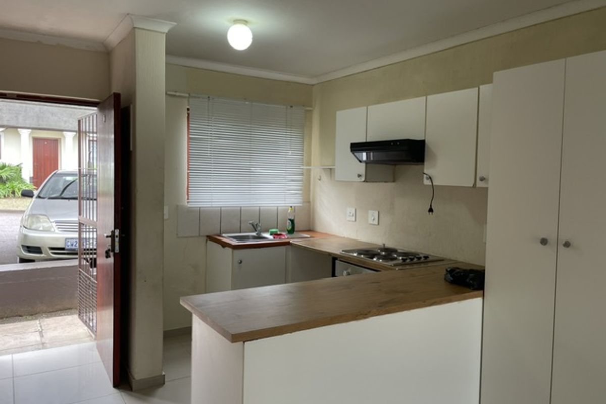 A compact kitchen featuring white cabinetry, a wood-look laminate countertop, built-in hob with extractor, and direct access to the exterior via a security gate.