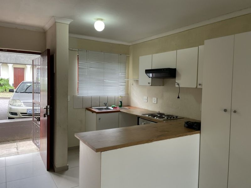 A compact kitchen featuring white cabinetry, a wood-look laminate countertop, built-in hob with extractor, and direct access to the exterior via a security gate.